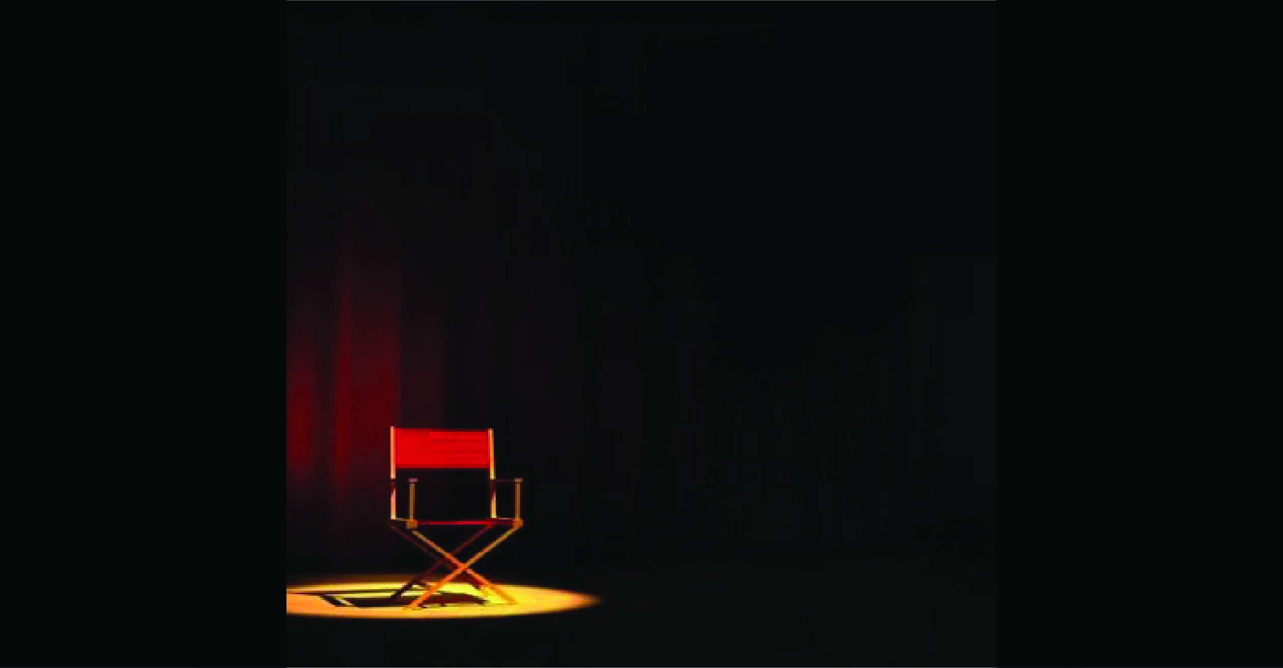 A red directing chair on a stage in a single spot light with a red curtain behind it.